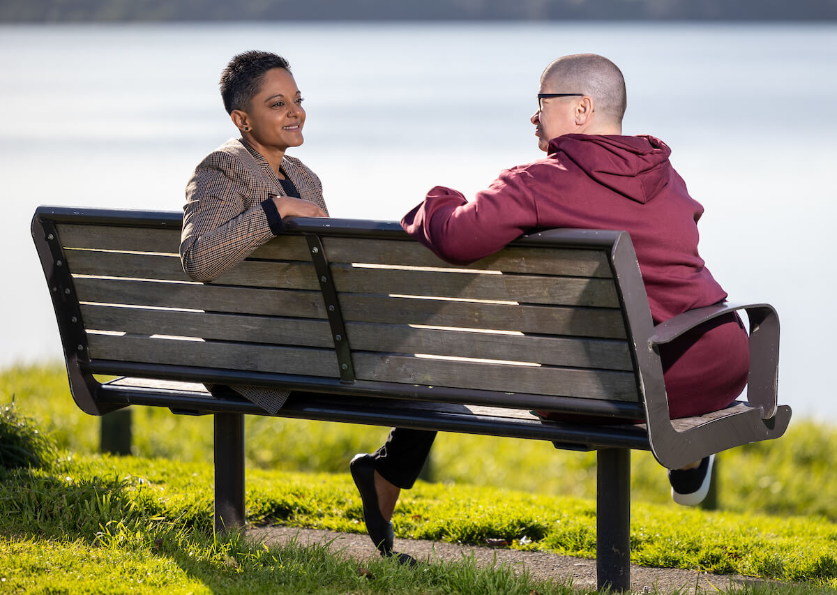 Beena Rugnathji chatting with a client on a park bench by the water.